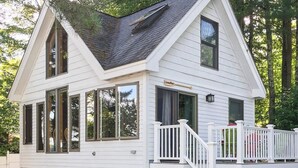 A two-story house with a gable roof, large windows, and a covered porch with a white railing. - Dog-Friendly Lakefront Cottage w/Lake Access, Deck, Gas Grill, A/C (Standish)
