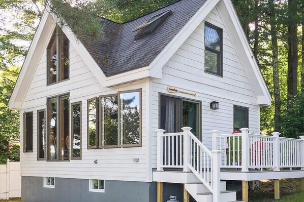 A two-story house with a gable roof, large windows, and a covered porch with a white railing.