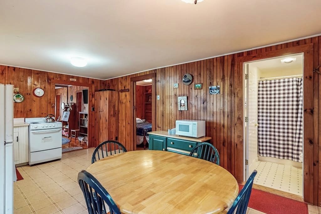 A wooden-paneled room with a kitchen, dining table, chairs, a microwave, and a checkered shower curtain.