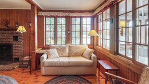 Una habitación acogedora con chimenea, un sofá, una mesa y ventanas amplias.