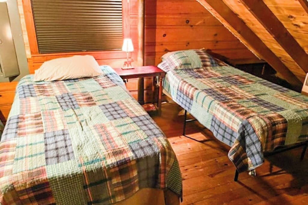 A small, cozy room with two single beds, a wooden ceiling, and a window with blinds.