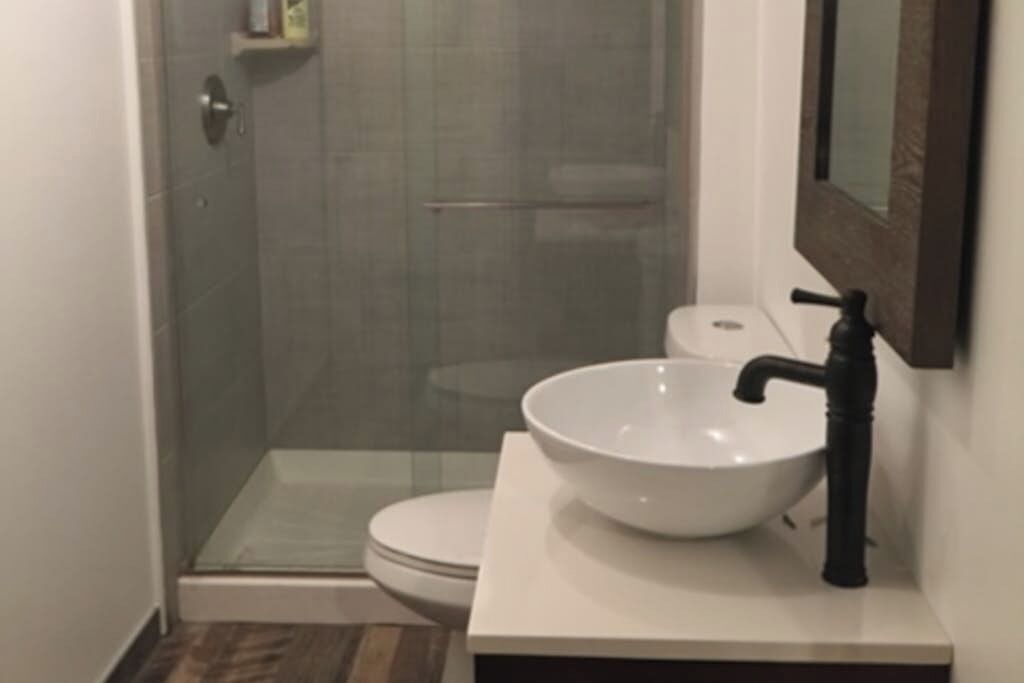 Een badkamer met een douchecabine van glas, een witte wastafel met een zwarte kraan, en een toilet.