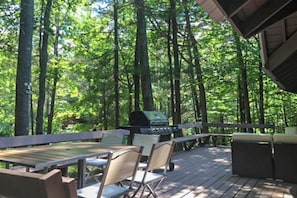 A deck with outdoor furniture, a grill, and a forested backdrop. - Private waterfront cabin with large deck, private dock, kayaks & gas grill (Naples)