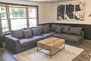 A living room with a gray sofa, a wooden coffee table, and a large abstract painting on the wall. - Private waterfront cabin with large deck, private dock, kayaks & gas grill (Naples)