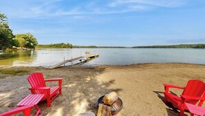 Un entorno junto al lago con sillas Adirondack rojas, un muelle y un brasero.
