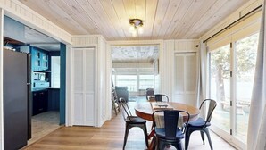 Un comedor con una mesa y sillas de madera, una cocina al fondo y ventanas amplias.