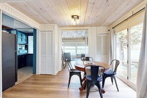 Un comedor con una mesa y sillas de madera, una cocina al fondo y ventanas amplias.