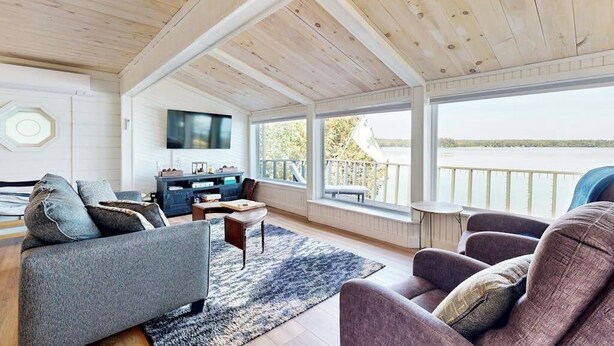 Amplia sala de estar con techo de madera, un televisor grande y vista a un lago.