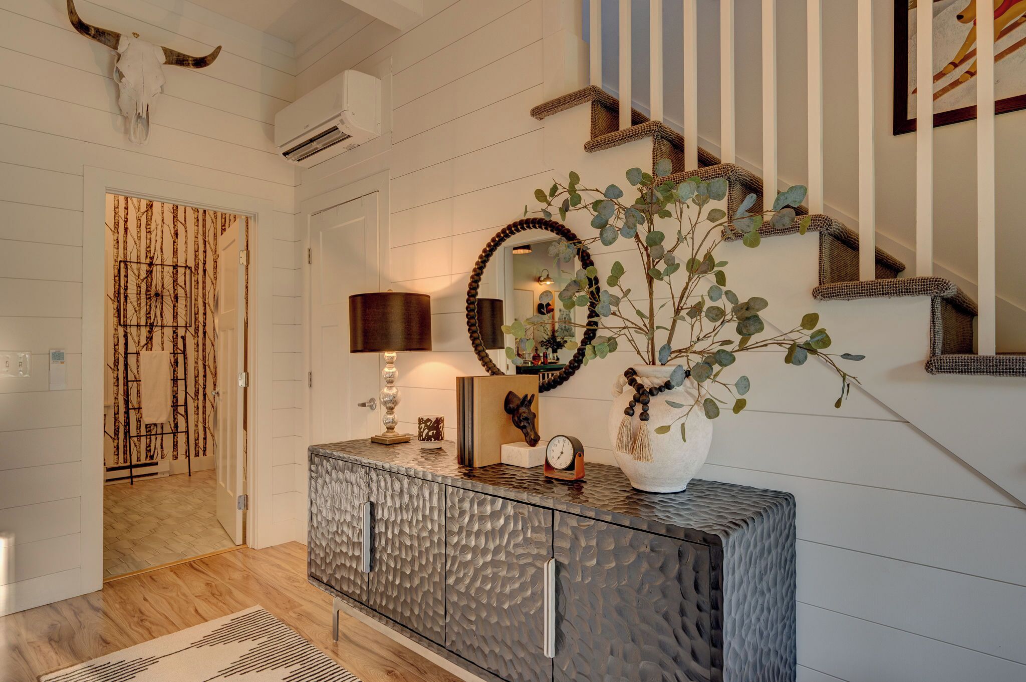 A hallway with a textured cabinet, a mirror, a clock, and a decorative plant.