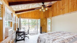 Quarto com cama, escrivaninha, cadeira, ventoinha no teto e janelas amplas.