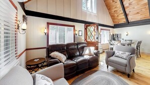 Uma sala de estar ampla com um sofá de couro, uma poltrona cinza e um espaço de jantar com mobiliário de madeira.