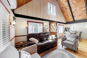 A spacious living room with a leather sofa, a grey armchair, and a dining area with wooden furniture.