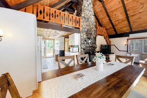 A wooden dining table with chairs, a stone pillar, and a television in a rustic interior.