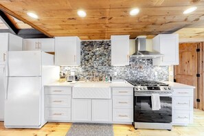 A kitchen with white cabinets, a stone backsplash, a gas stove, and a built-in oven.