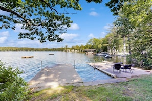 A lakeside dock with a concrete platform, a small boat, and a row of chairs. - Naples Lakefront Retreat | Private Beach, Dock & Kayaks | Family + Dog friendly (Naples)