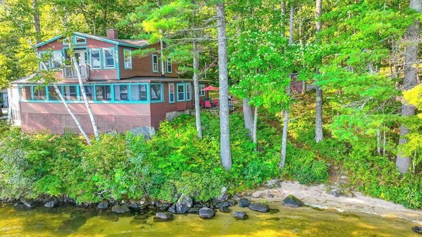 Una casa junto a un río con un muelle, rodeada de árboles frondosos.