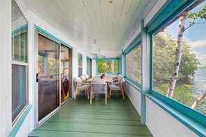 A covered porch with a table and chairs, large windows, and a view of a body of water.