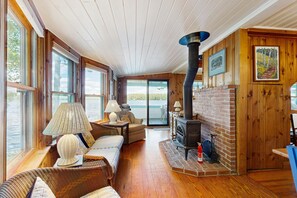A cozy room with a fireplace, wooden walls, and large windows.