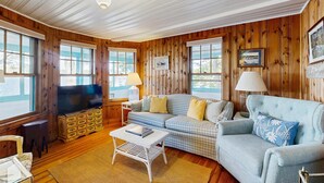 Una sala de estar acogedora con paredes de madera, un sofá azul, un televisor y una mesa de centro.