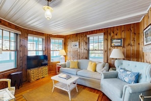 A cozy living room with wooden walls, a blue sofa, a television, and a coffee table. - Naples Lakefront Retreat | Private Beach, Dock & Kayaks | Family + Dog friendly (Naples)