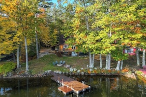 Eine Blockhütte am See mit einer Anlegestelle, umgeben von Herbstlaub.