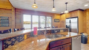 A kitchen with granite countertops, wooden cabinets, a stainless steel sink, and a refrigerator. - Lakefront, dog-friendly home with dock, kayaks, SUPs, canoe, huge deck & firepit (Norway)