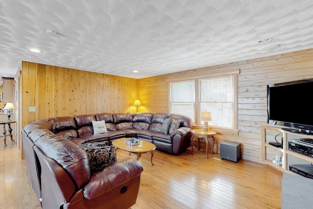 Un salon avec un canapé d’angle, une table basse, un téléviseur et des murs en bois.