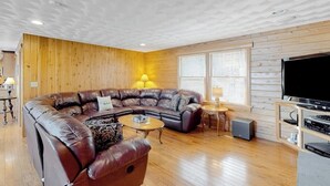 A living room with a sectional sofa, a coffee table, a TV, and wooden walls. - Lakefront, dog-friendly home with dock, kayaks, SUPs, canoe, huge deck & firepit (Norway)
