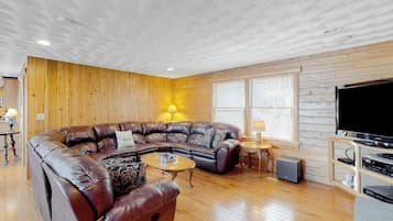 Un salon avec un canapé d’angle, une table basse, un téléviseur et des murs en bois.