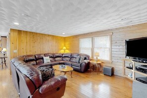 Ein Wohnzimmer mit einer Eckcouch, einem Couchtisch, einem Fernseher und Holzwänden.