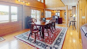 A wooden cabin interior with a dining area, large windows, and a view of the outdoors. - Lakefront, dog-friendly home with dock, kayaks, SUPs, canoe, huge deck & firepit (Norway)