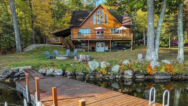 A cabin with a dock extending into a lake, surrounded by trees and a stone wall. - Lakefront, dog-friendly home with dock, kayaks, SUPs, canoe, huge deck & firepit (Norway)