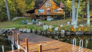 Une cabane avec un quai s’avançant dans un lac, entourée d’arbres et d’un mur de pierres.