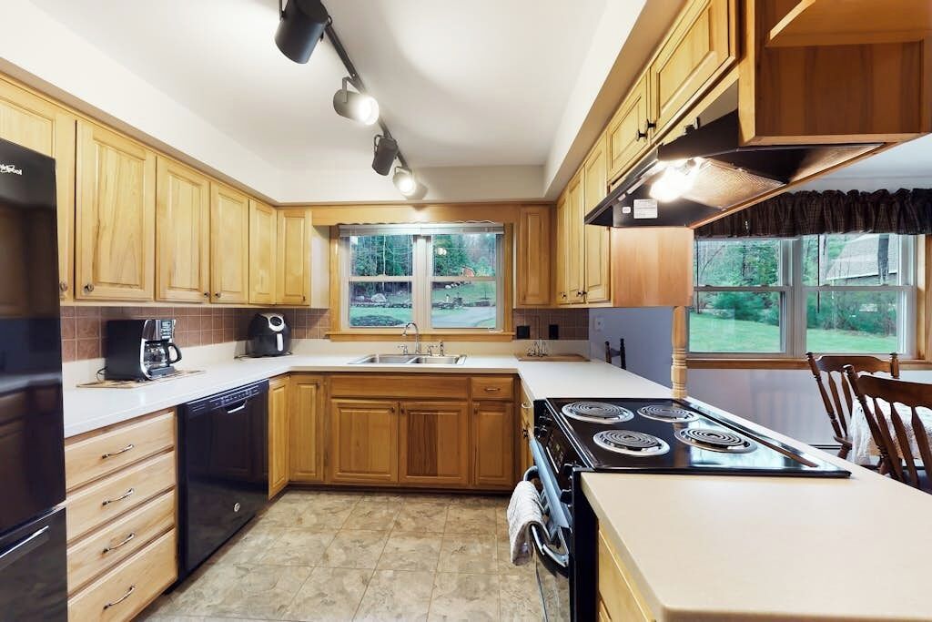 A kitchen with wooden cabinets, a stove, a dishwasher, and a window with a view of greenery.