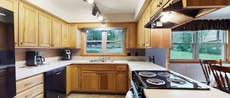 A kitchen with wooden cabinets, a stove, a dishwasher, and a window with a view of greenery.