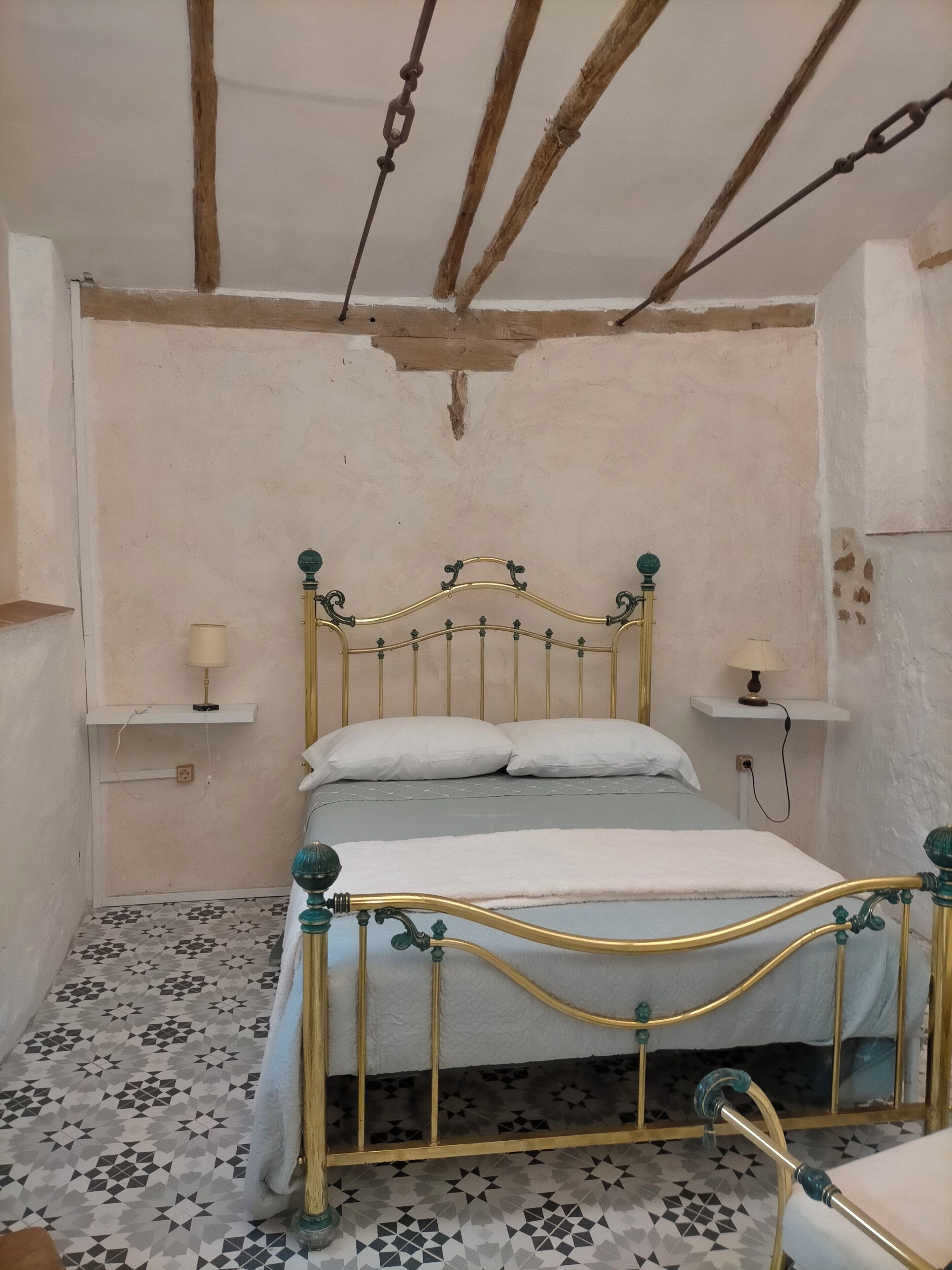 Une chambre avec un lit, deux tables de chevet avec des lampes, un sol à motifs et des poutres en bois apparentes au plafond.