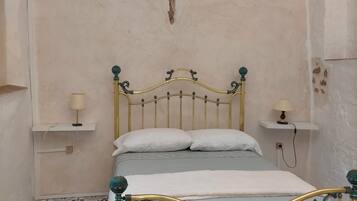 Una habitación con cama, dos mesitas de noche con lámparas, suelo estampado y vigas de madera a la vista en el techo.