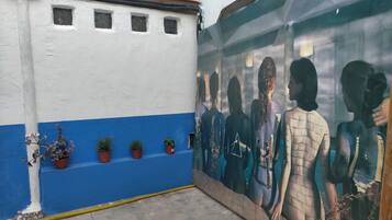 Un edificio con fachada azul y blanca, plantas en macetas en la pared baja y un mural a la derecha.