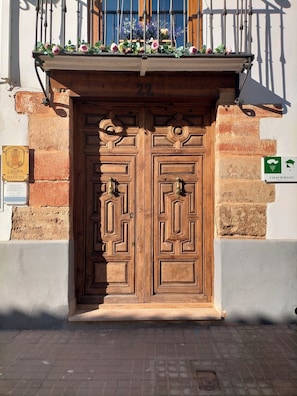 Una puerta doble de madera con el número '22' encima, un balcón con flores y un cartel que indica 'CASA RURAL'.