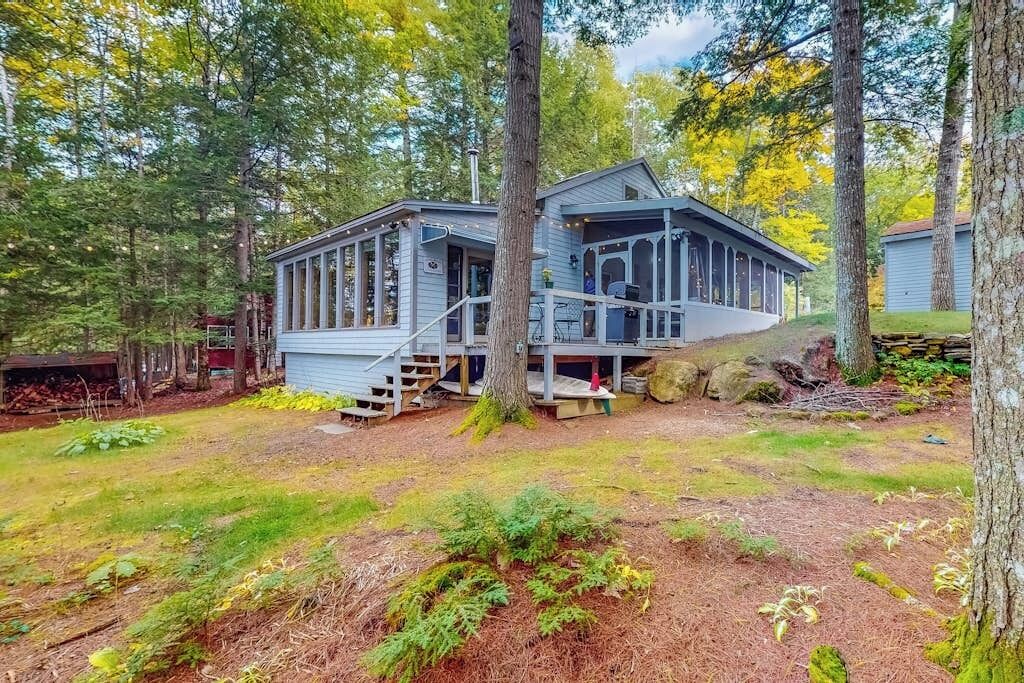 A cabin with a porch, surrounded by trees and a grassy yard.