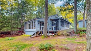Een chalet met een veranda, omringd door bomen en een gazon.