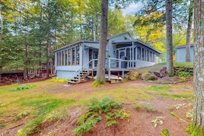 Eine Hütte mit Veranda, umgeben von Bäumen und einem Rasen.