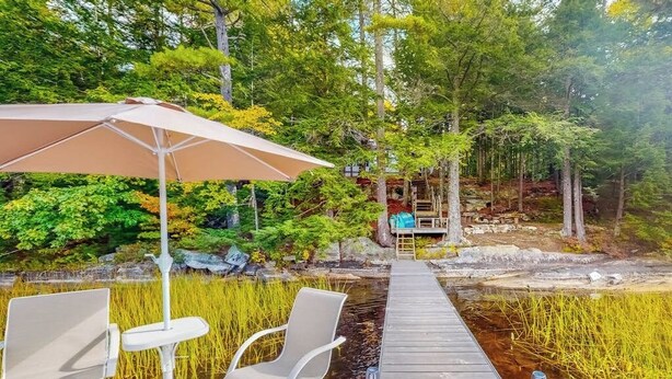 Een houten steiger die uitkomt bij een vijver, met stoelen en een parasol.