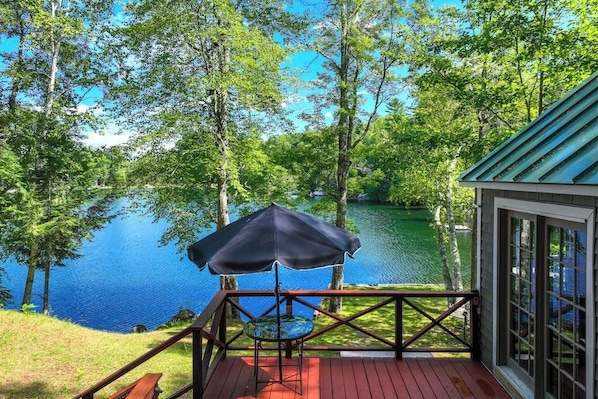 A deck with a table and umbrella overlooking a lake, surrounded by trees.
