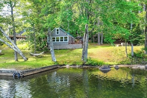 A lakeside cabin with a deck, surrounded by trees and a small dock.