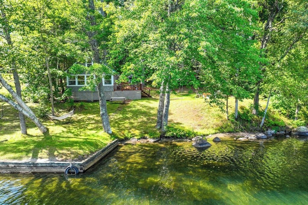 A lakeside cabin with a dock, surrounded by dense trees and a grassy area.