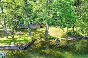 A lakeside cabin with a dock, surrounded by dense trees and a grassy area.