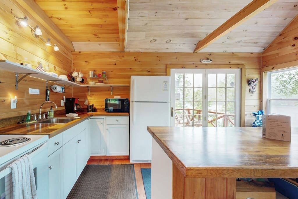 L’intérieur d’un chalet en bois comprend un coin cuisine, une table à manger et une vue sur l’extérieur, visible à travers la porte.
