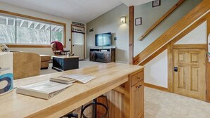 A room with a wooden desk, a television, a staircase, and a window with blinds. - Ski-in/out 2-story condo with balcony, on-site indoor pool, hot tub, sauna, W/D (Newry)