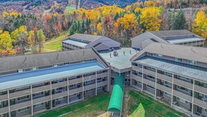 A multi-story building with a central courtyard, surrounded by autumn-colored trees and a mountainous backdrop. - Ski-in/out 2-story condo with balcony, on-site indoor pool, hot tub, sauna, W/D (Newry)
